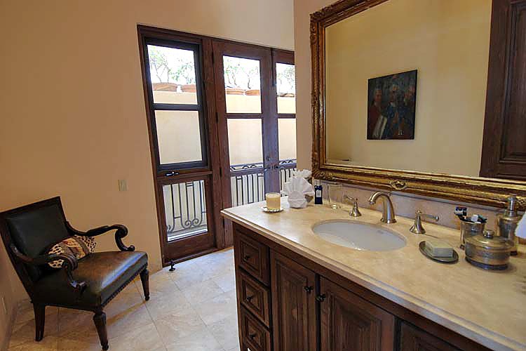 Elegant bathroom with a large mirror above a wooden vanity, a decorative chair, and natural light from glass doors.