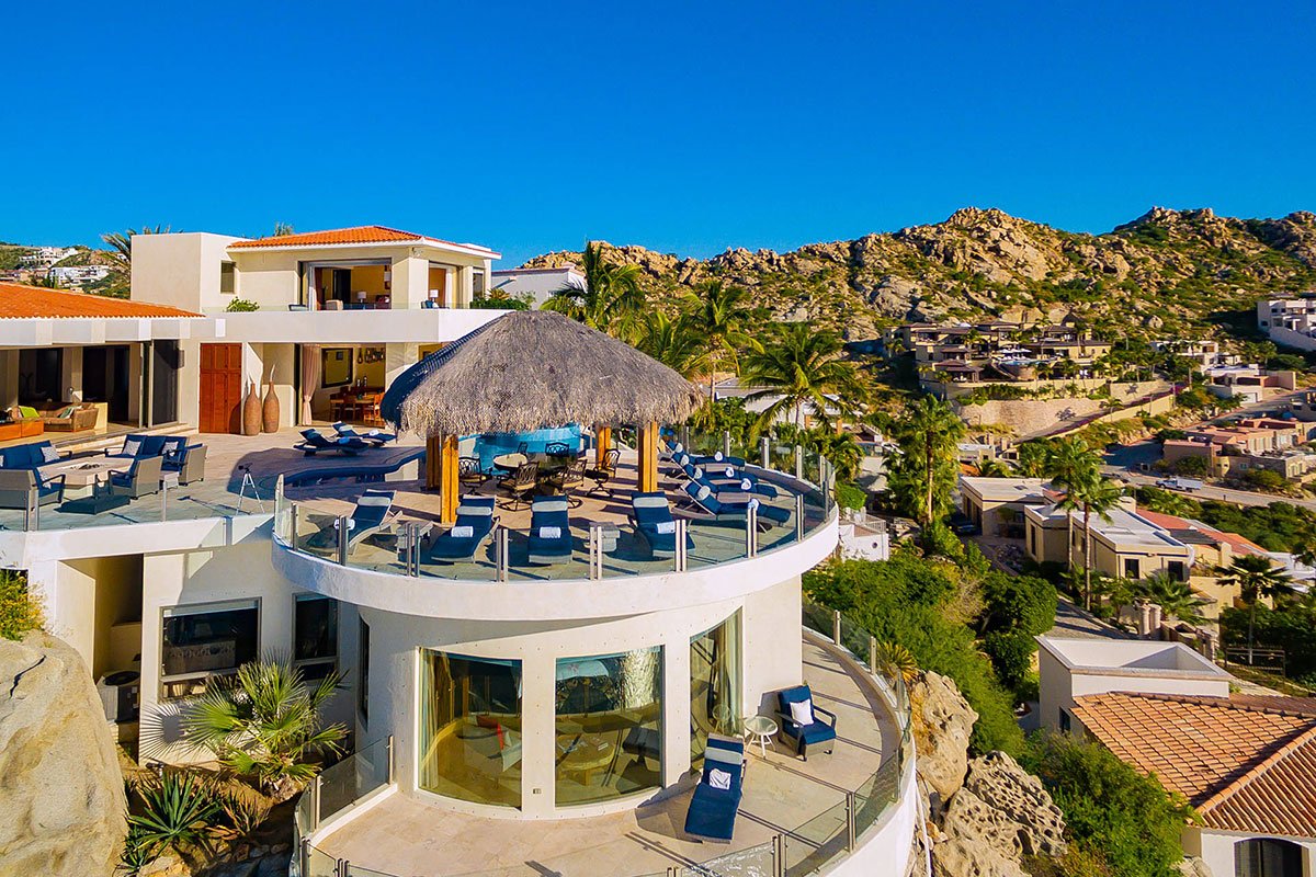 Luxury villa with a thatched-roof patio, pool chairs, and panoramic views in a mountainous region.