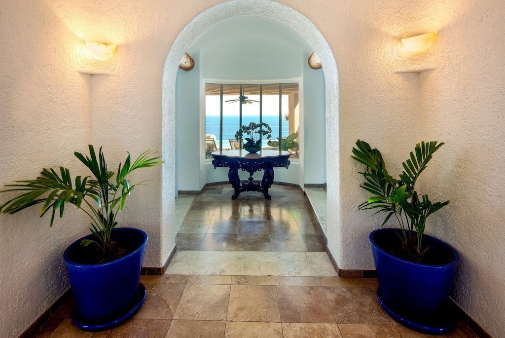 Interior hallway with arched doorway, two potted plants, and a table, leading to windows with ocean view.