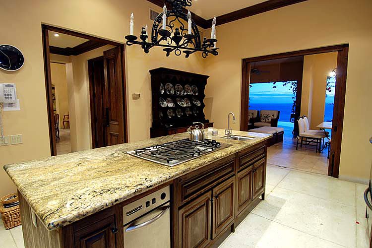 Luxurious kitchen with granite island, gas stove, and elegant chandelier, open to ocean view dining area.