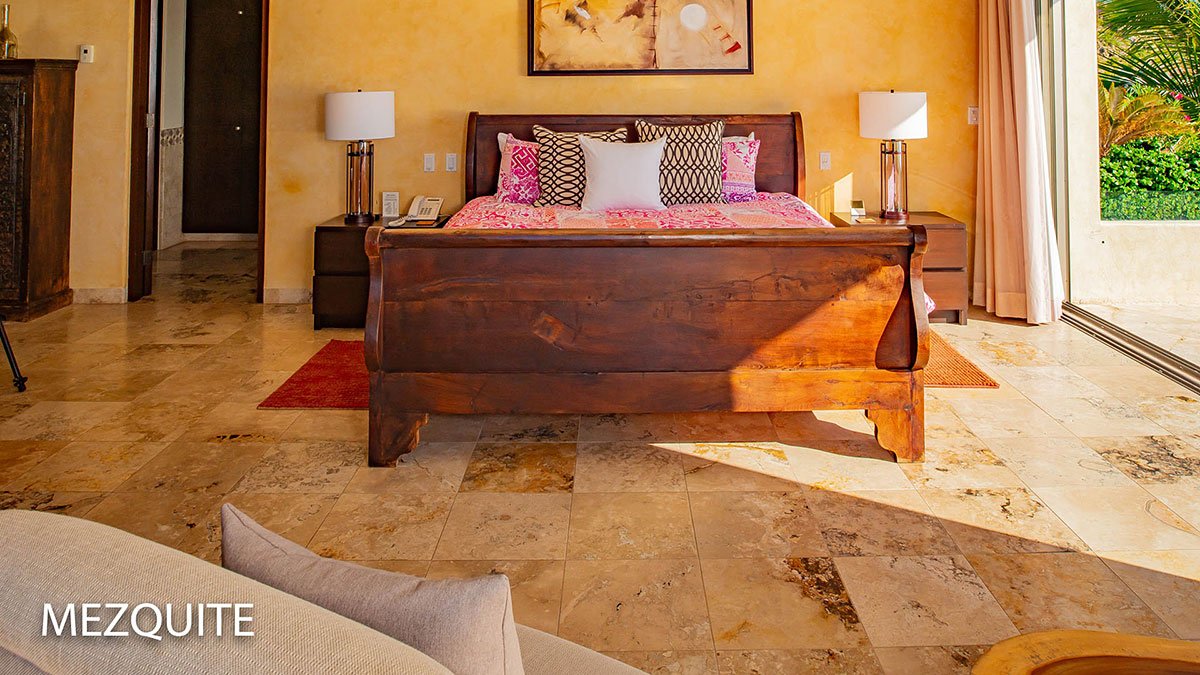 Modern bedroom with wooden bed, colorful bedding, two bedside tables with lamps, tiled floor, wall art, and an open door leading to a garden view.
