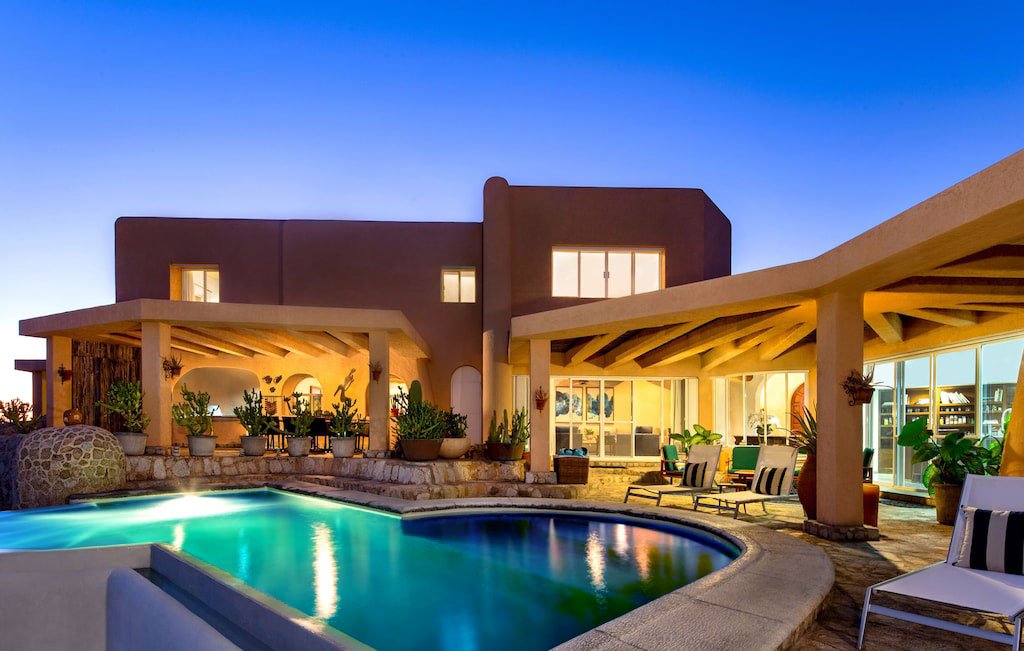 Luxury villa with pool and patio at sunset, featuring modern architecture and outdoor furniture.