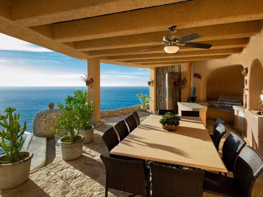 Outdoor patio overlooking the ocean with a dining table, chairs, ceiling fan, and potted cacti.