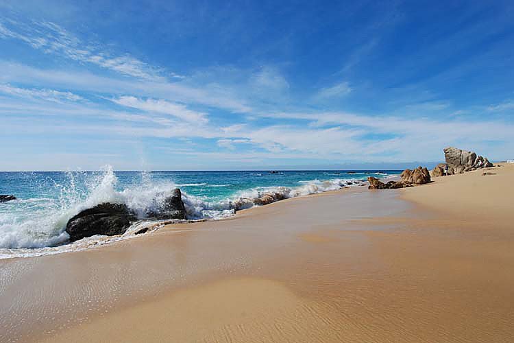 Sandy beach with rock formations, ocean waves and blue sky.