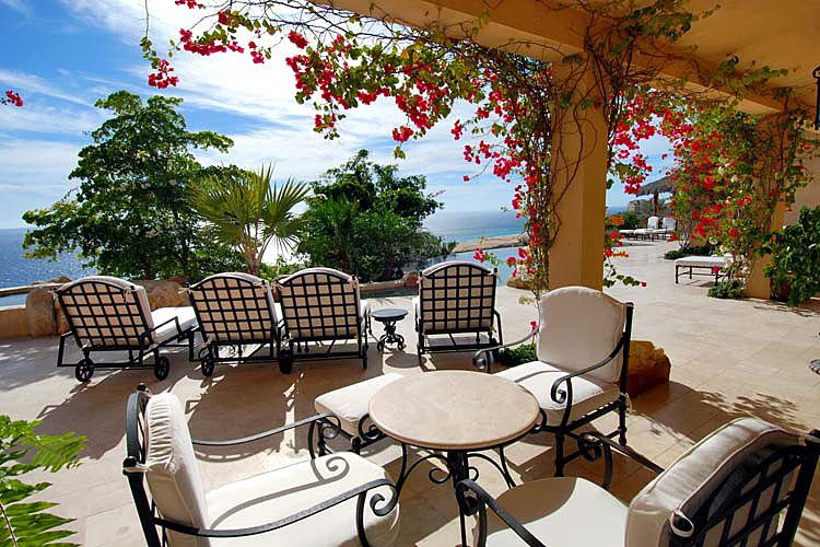 Luxury oceanfront patio with lounge chairs, dining table, and red flowering vines.