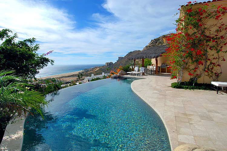 Infinity pool with ocean view, surrounded by a patio and greenery.