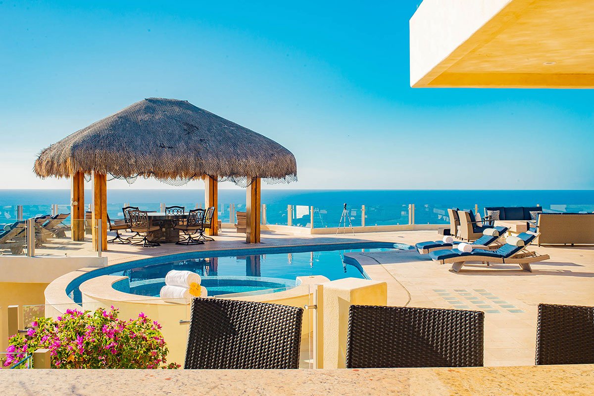 Luxury poolside area with ocean view, featuring a thatched-roof gazebo, sun loungers, and patio furniture.