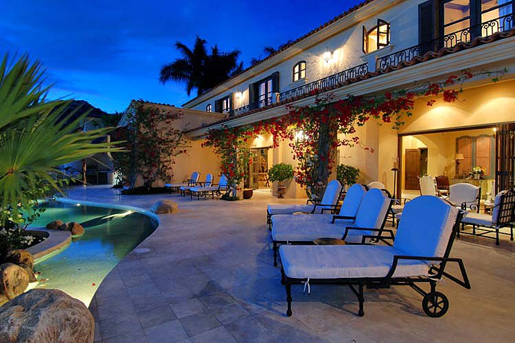 Luxury villa with a poolside patio, lounge chairs, and vibrant lighting at dusk.
