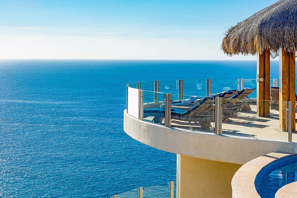 Ocean view from a luxury resort terrace with lounge chairs and a thatched roof canopy, overlooking the sea.