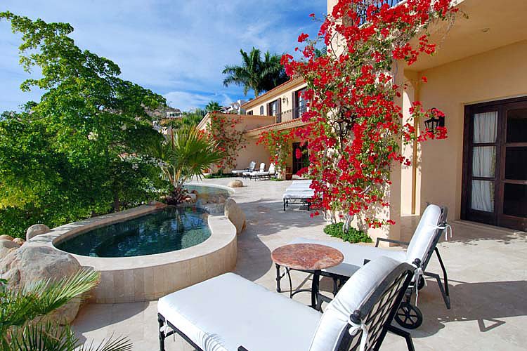 Luxury villa patio with pool, lounge chairs, and vibrant bougainvillea flowers.