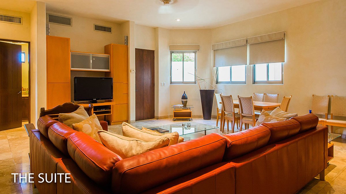 Living room with a red leather sectional sofa, wooden TV unit, flat-screen TV, dining table with chairs, and large windows with blinds.