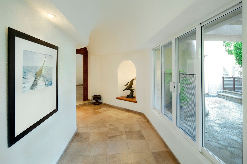 Bright hallway with tiled floor, featuring a framed picture of a marlin on the left wall, a marlin sculpture on a corner shelf, and large glass sliding doors on the right opening to a patio.