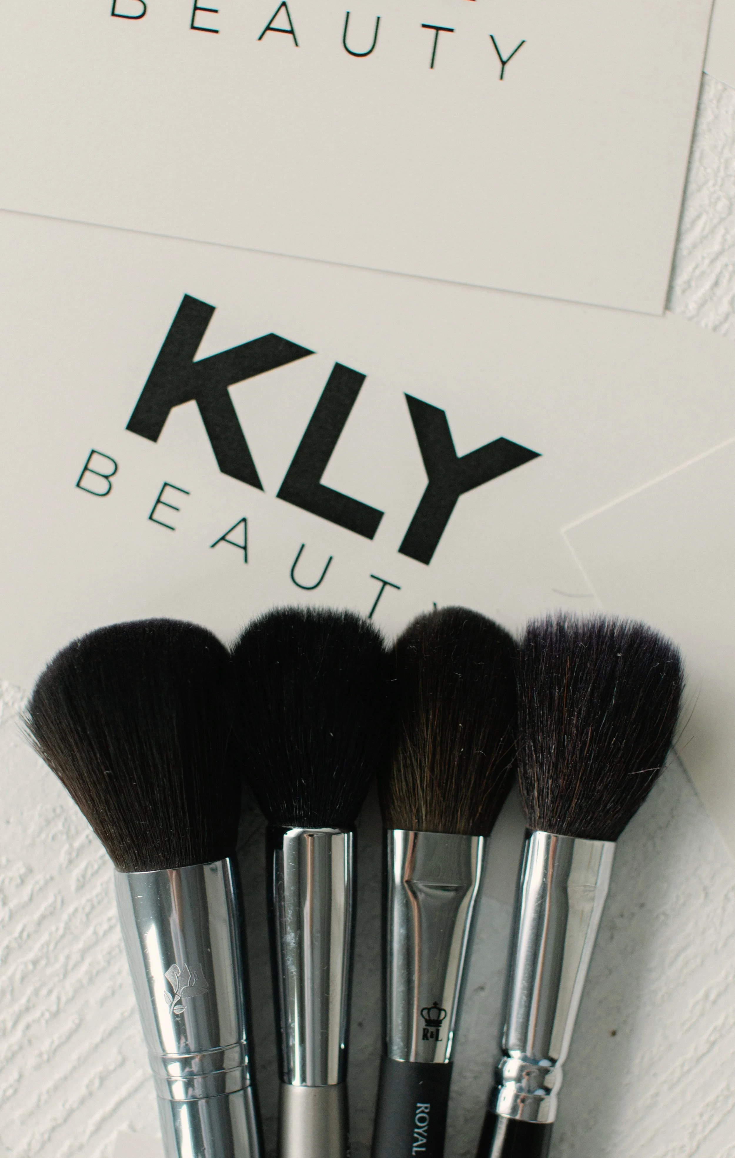 Four makeup brushes with black bristles on a white background, next to a sign reading "KLY Beauty."