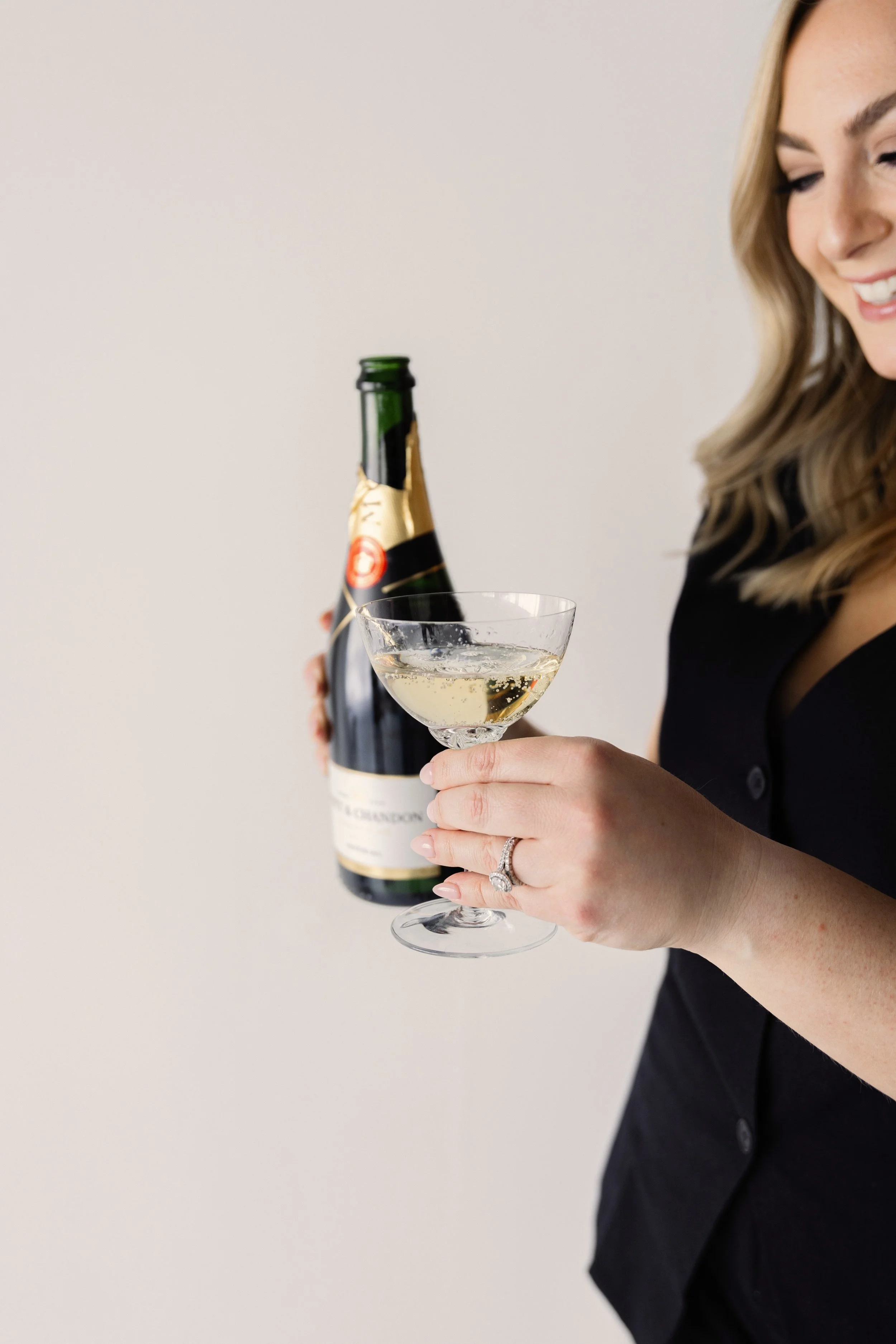 Person holding a bottle of champagne and a filled champagne glass, smiling.