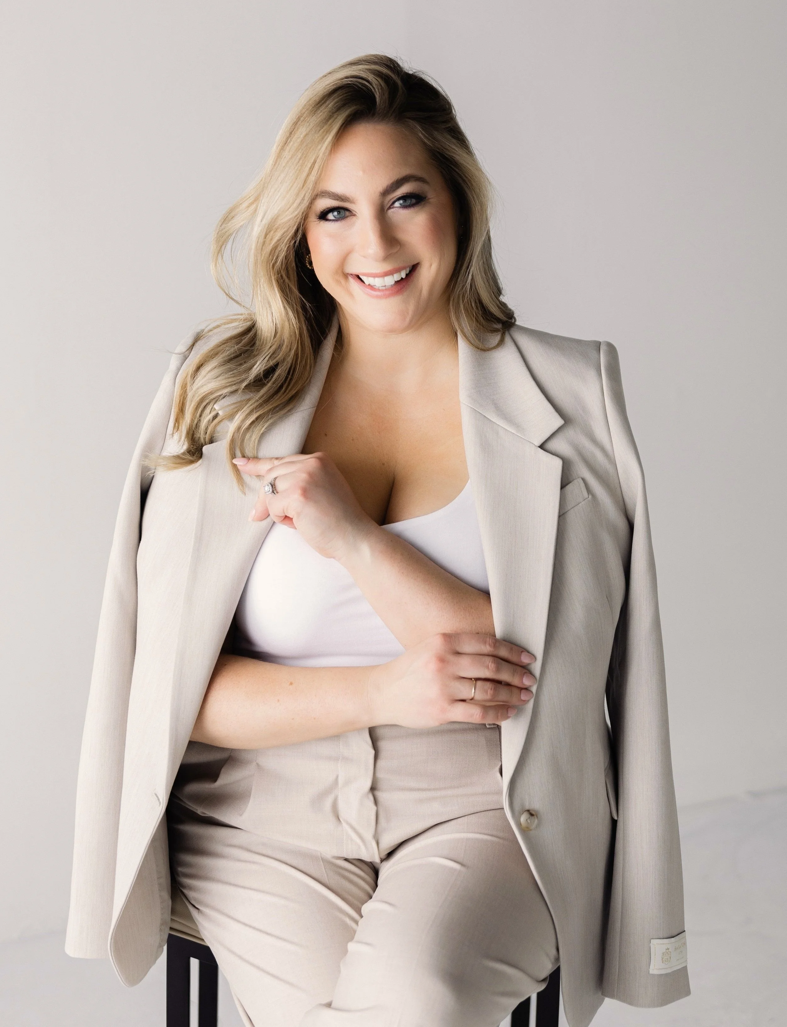 Smiling woman in a beige suit seated against a light background.