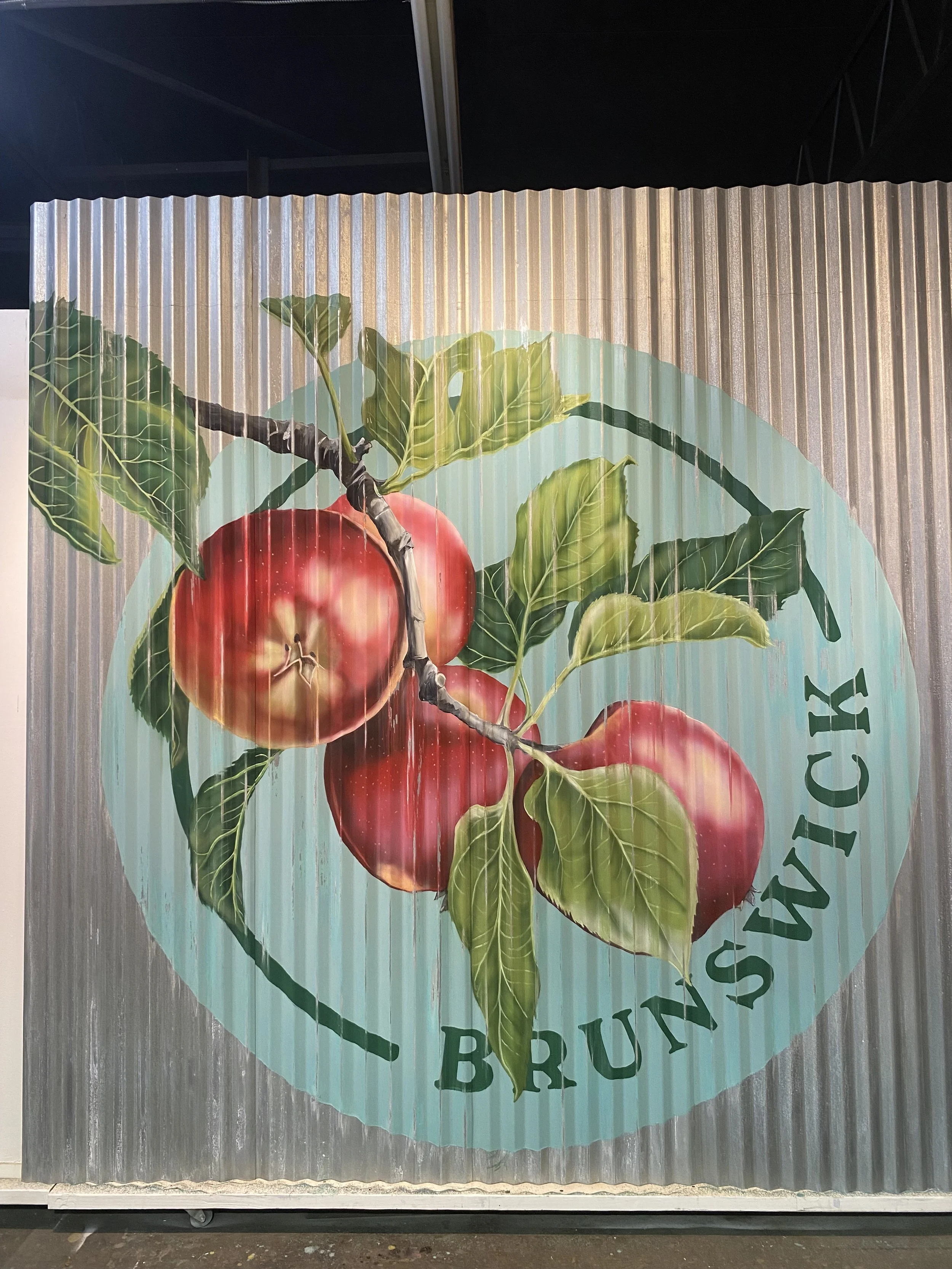 A painted mural of three red apples with green leaves on a branch, with the text 'Brunswick' on a circular background.