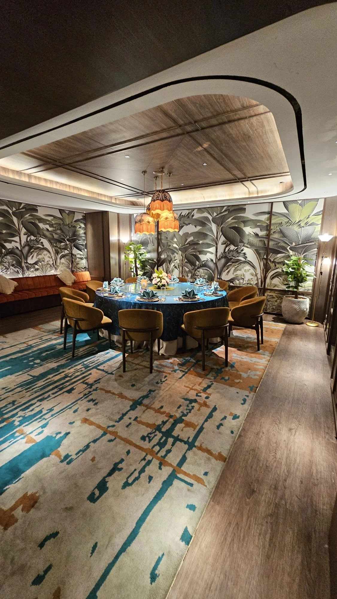 A round table set for a formal meal in a decorated dining room with wallpaper, plants, and ambient lighting.