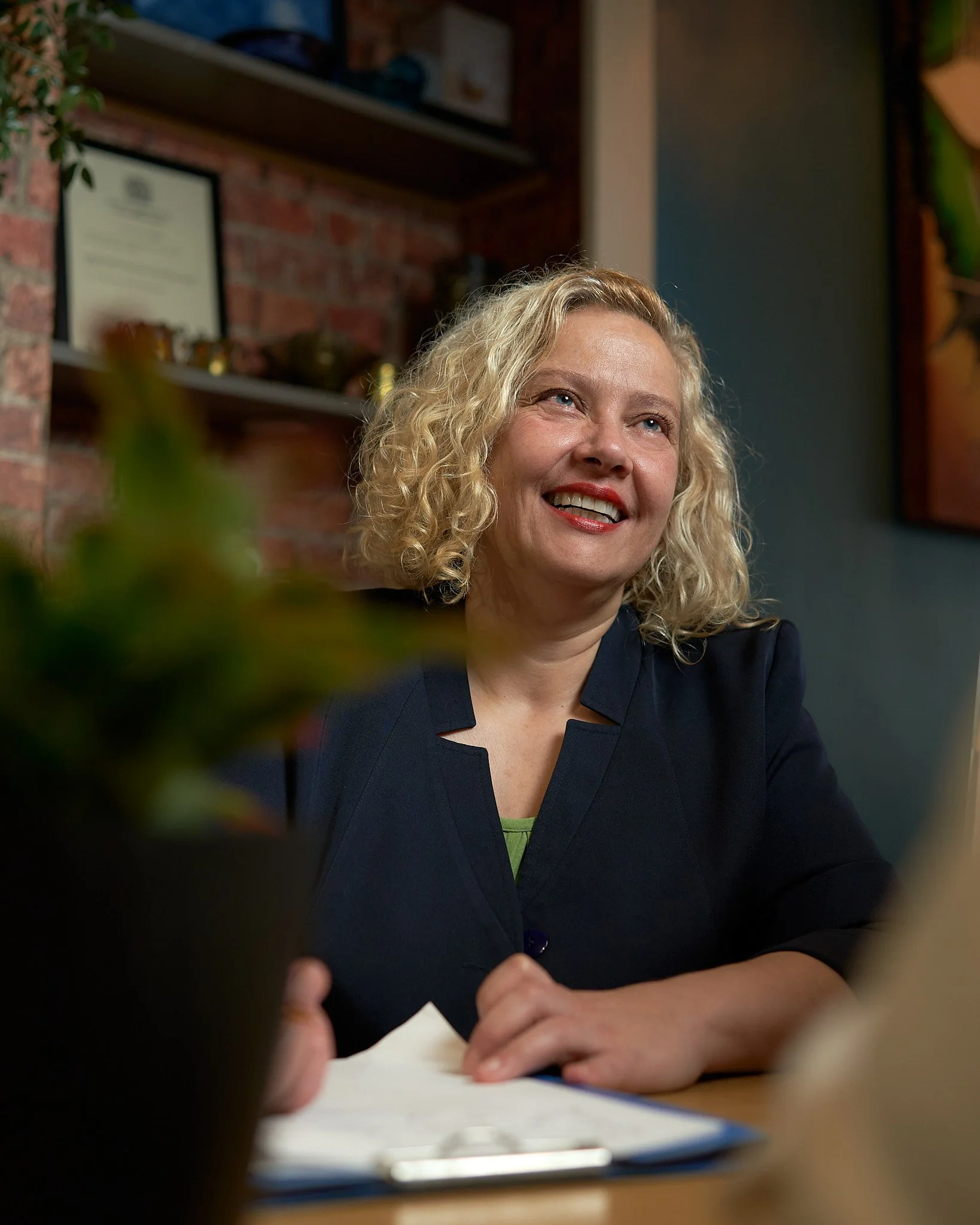 A woman with curly blonde hair smiling during a conversation in an office setting.