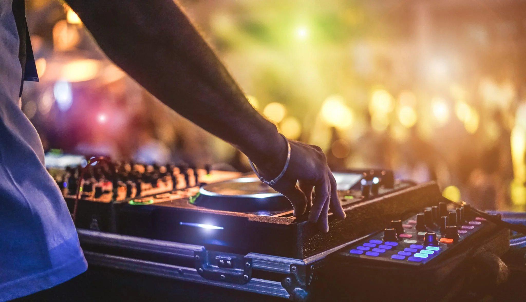 DJ mixing music at a party with colorful background lights.