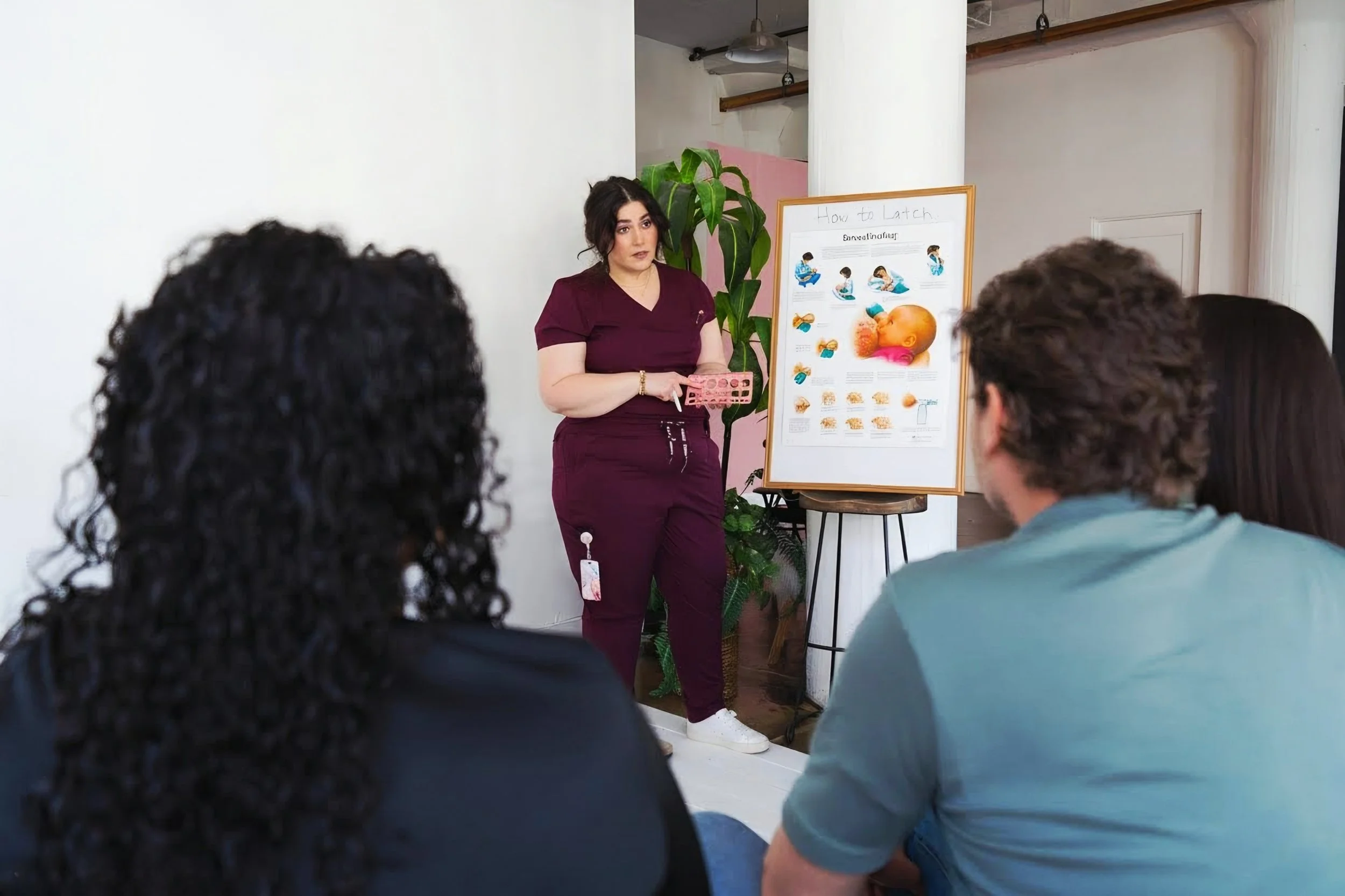 doula Jorie teaching a class for a group of soon to be parents. She has a poster sign describing ways to breasfeed.