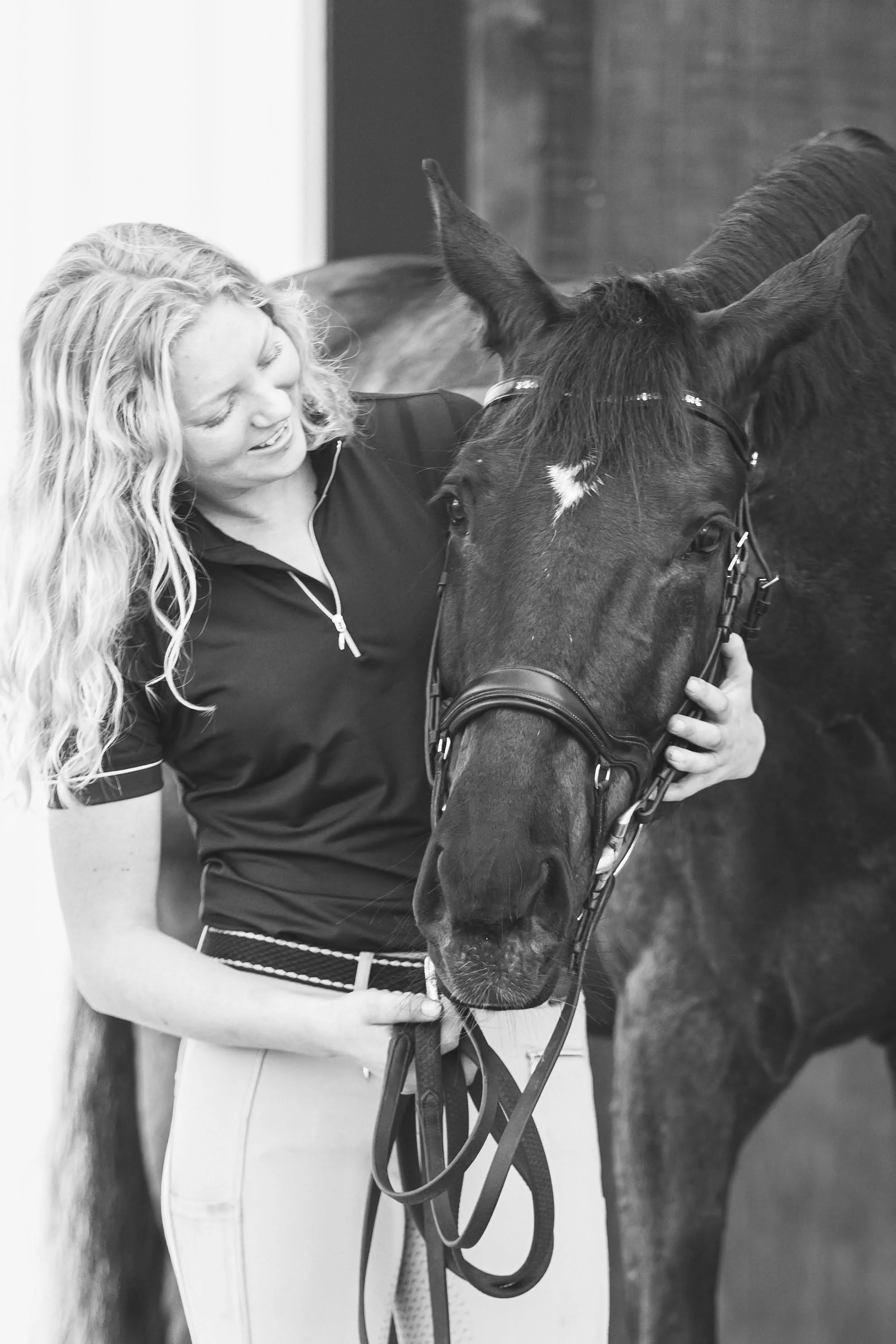 Woman smiling and hugging a dark horse in a stable.