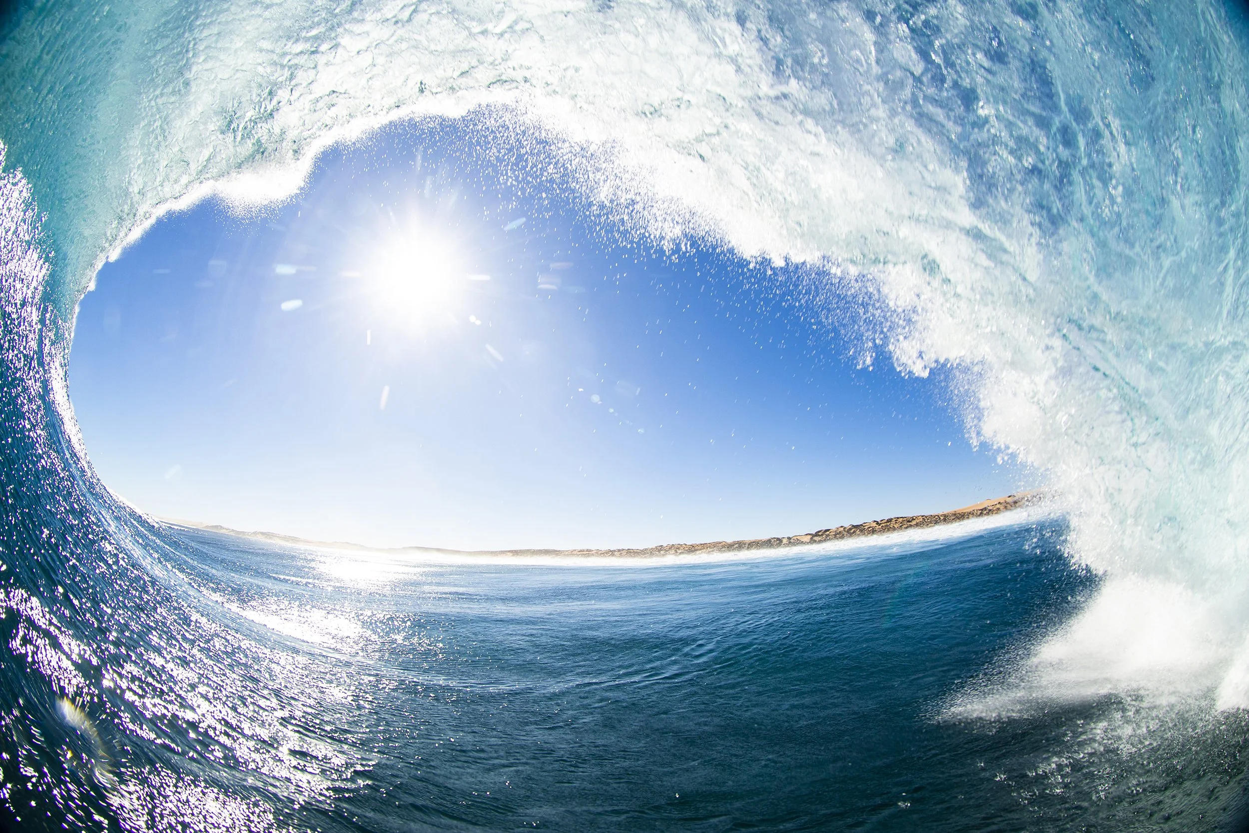 Inside view of a breaking ocean wave with sunlight shining in a clear blue sky.