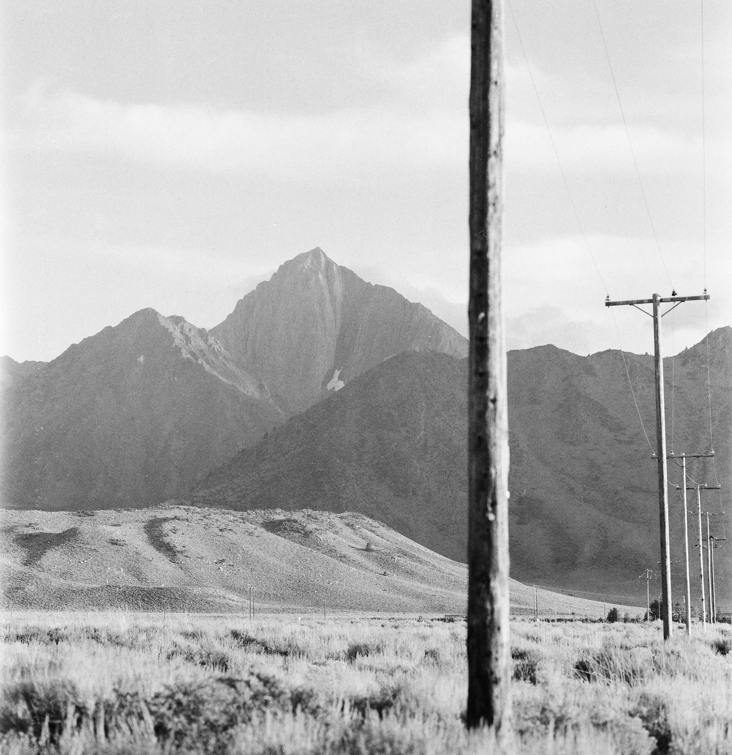 Black and white landscape with mountains, transmission poles, and grass field.