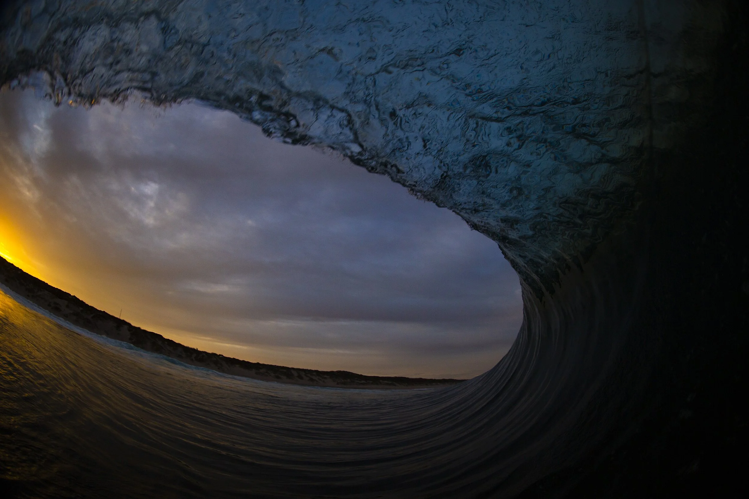 Inside view of a crashing ocean wave at sunset with blue and orange sky.