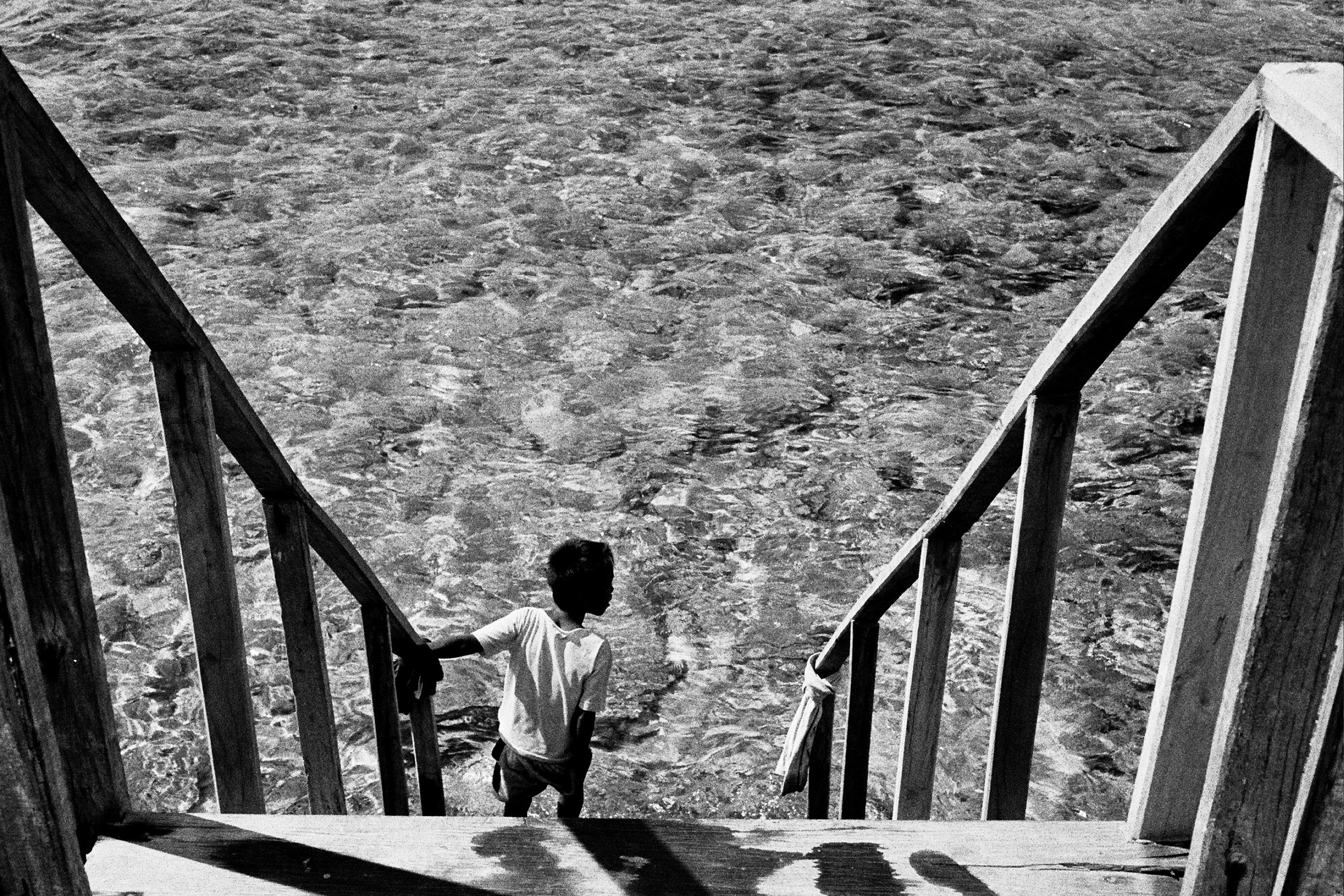 Child standing on wooden stairs leading to clear water