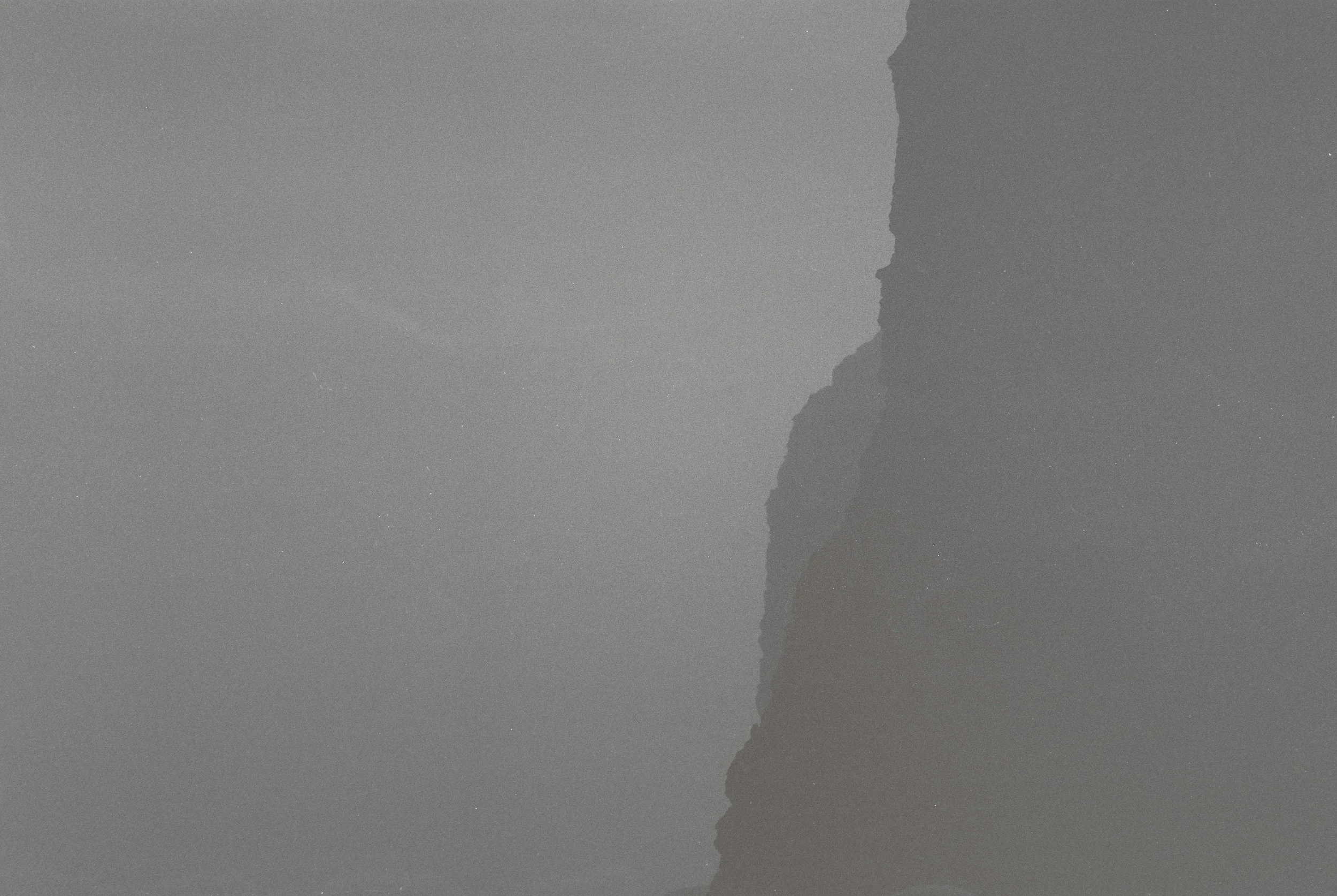 Monochrome abstract image with textured surface and shadowy shapes on the right.