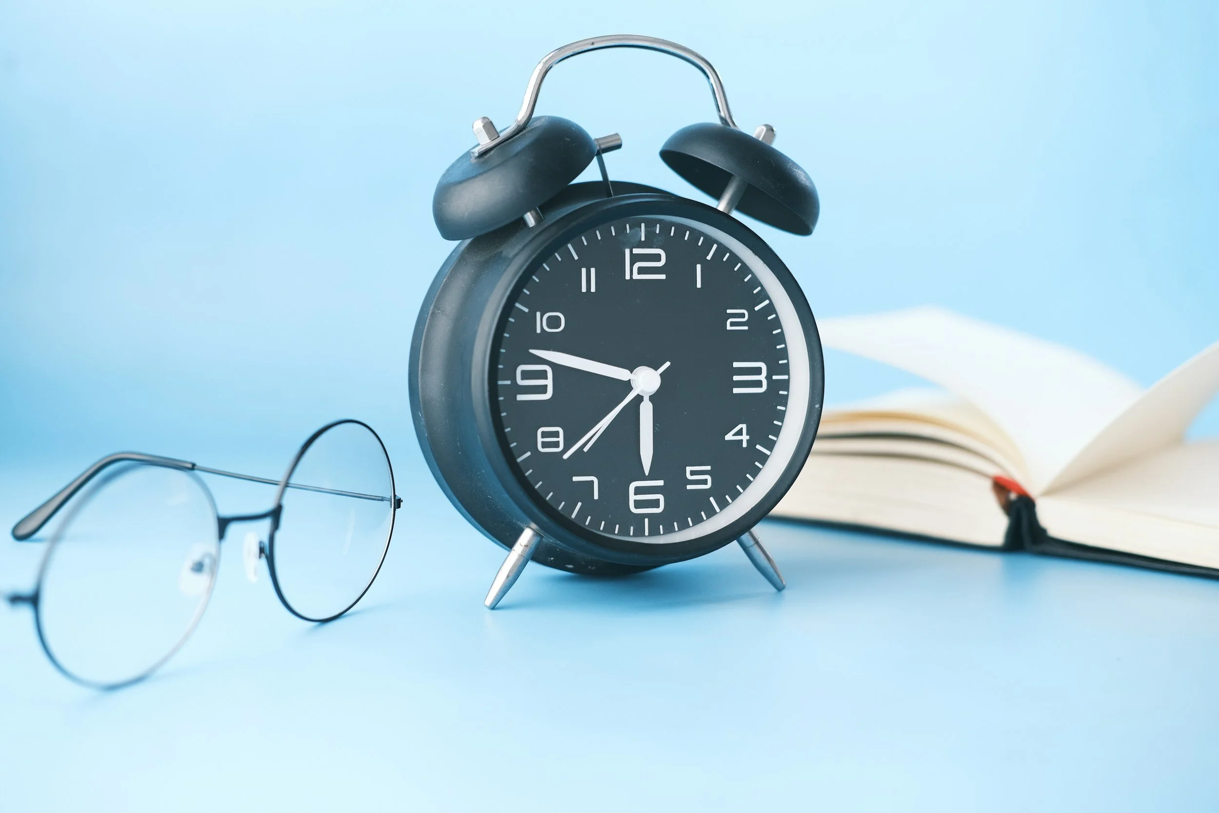 A clock, glasses, and book against a blue background.