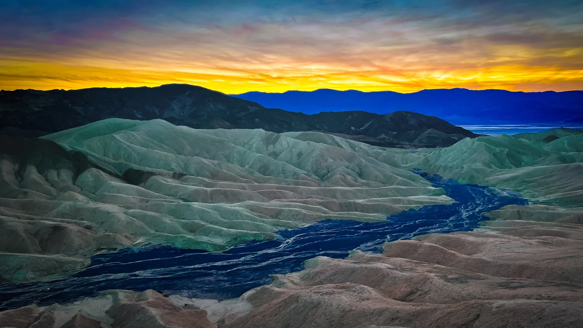 Colorful landscape of mountains, river, and a sunset sky with vibrant colors.