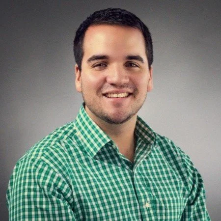 Smiling man wearing a green checkered shirt against a gray background.
