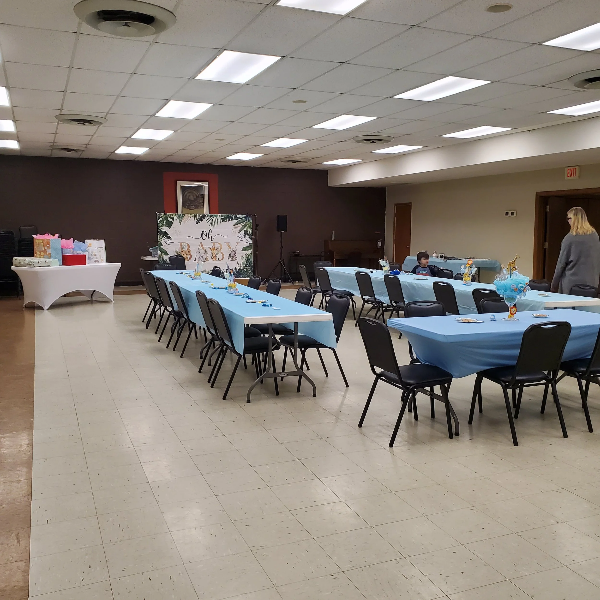 Church baby shower decorated with K&D Hospitality Services rentals, including blue tablecloths, a Oh Baby backdrop, and a styled gift table.