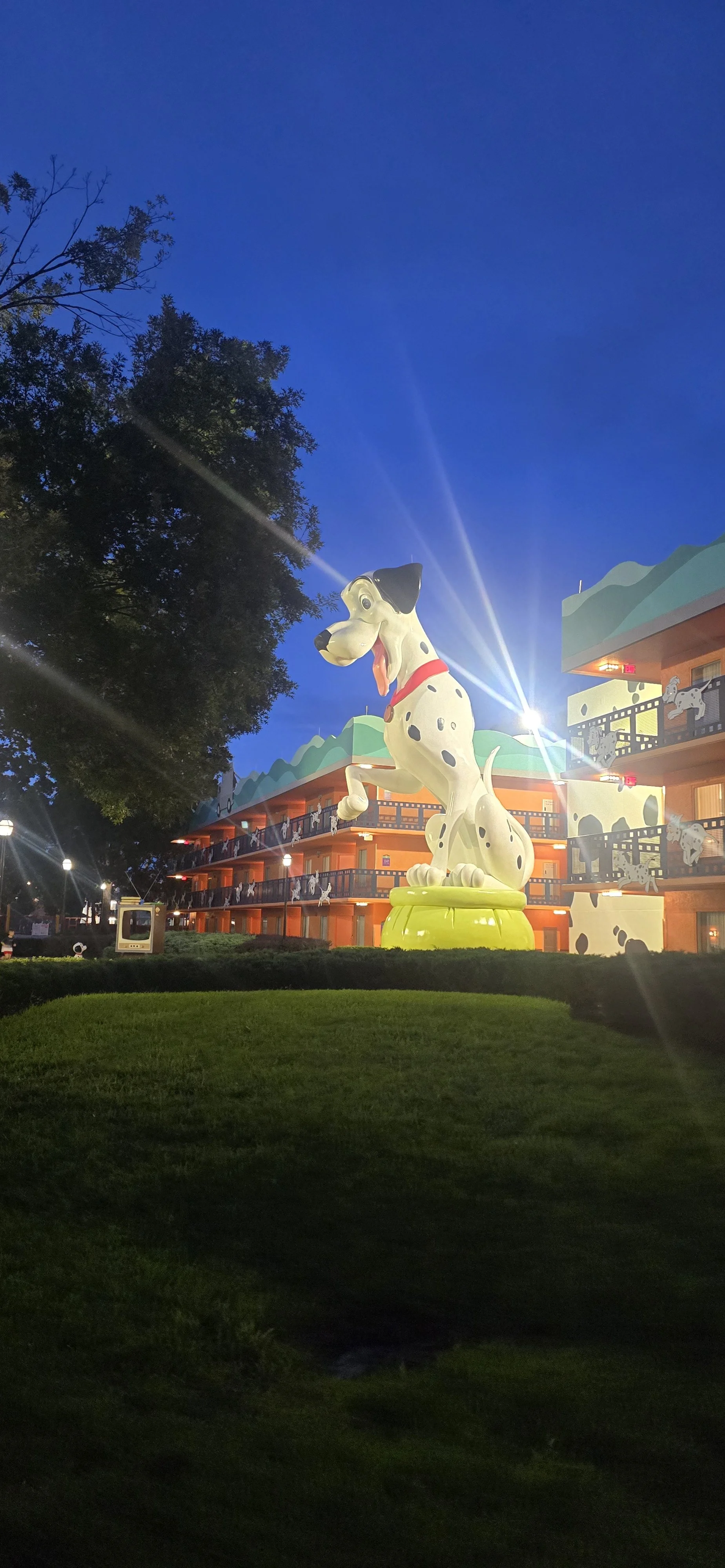 Disney’s All-Star Movies Resort at night with a giant Dalmatian character statue, themed hotel buildings, and bright spotlights in the background.