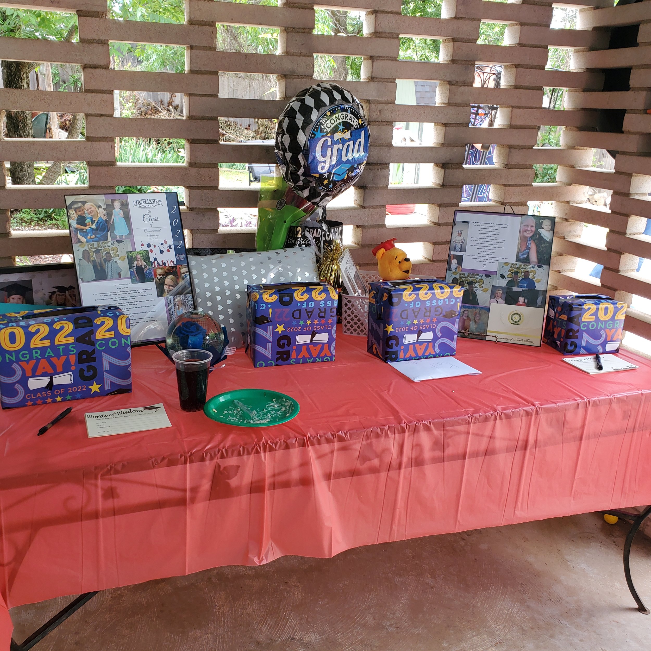 Graduation gift table with photos of both graduates, balloons, wrapped gifts, card boxes, and handwritten notes for the graduates.