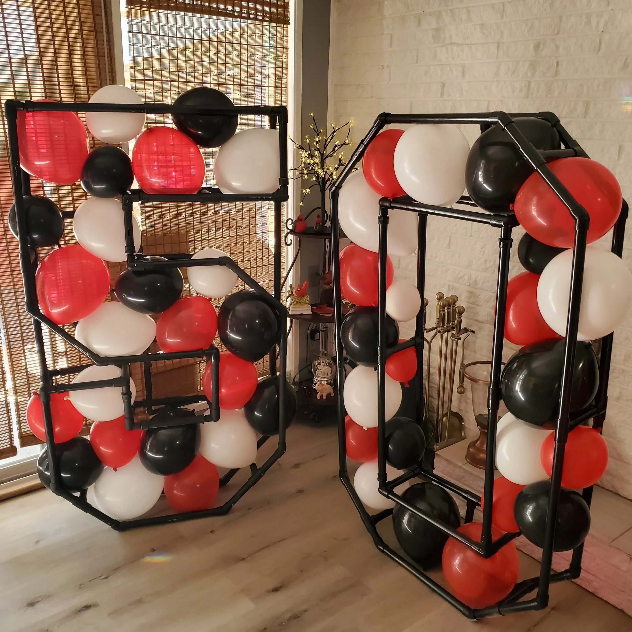 A display of black, white, and red balloons arranged around black metal shelves in a room with a wooden floor and bamboo window blinds.