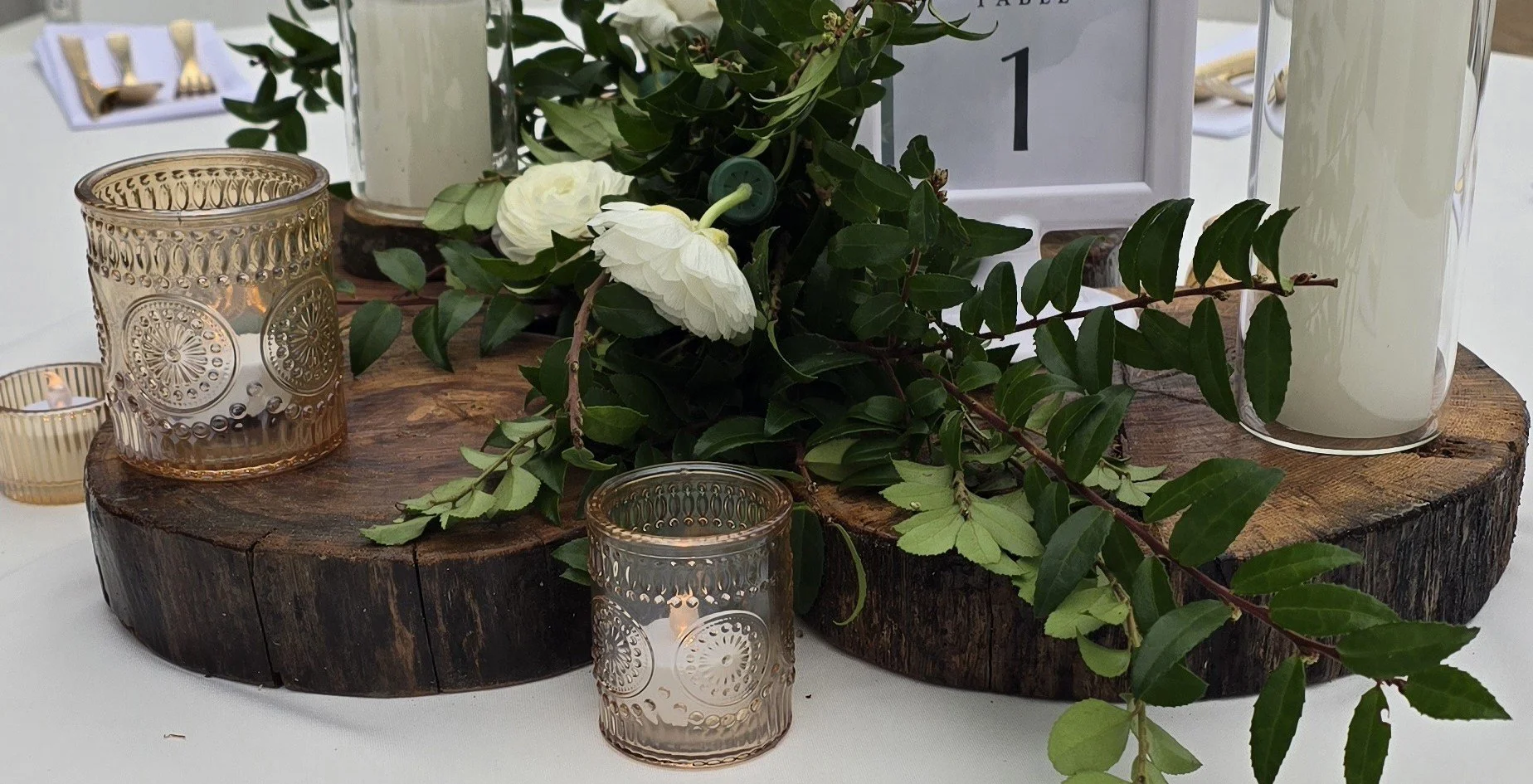 Wedding centerpiece featuring K&D Hospitality Services candle holders, gold votives, handcrafted wood risers, and floral décor arranged for the reception table.