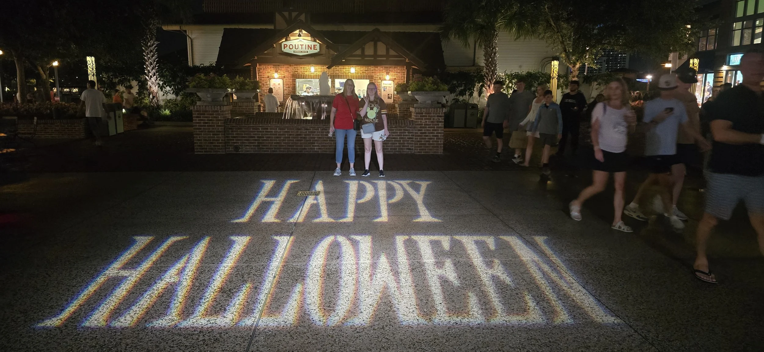 Guests at Walt Disney World during Mickey’s Not-So-Scary Halloween Party with “Happy Halloween” projected across the walkway at night.