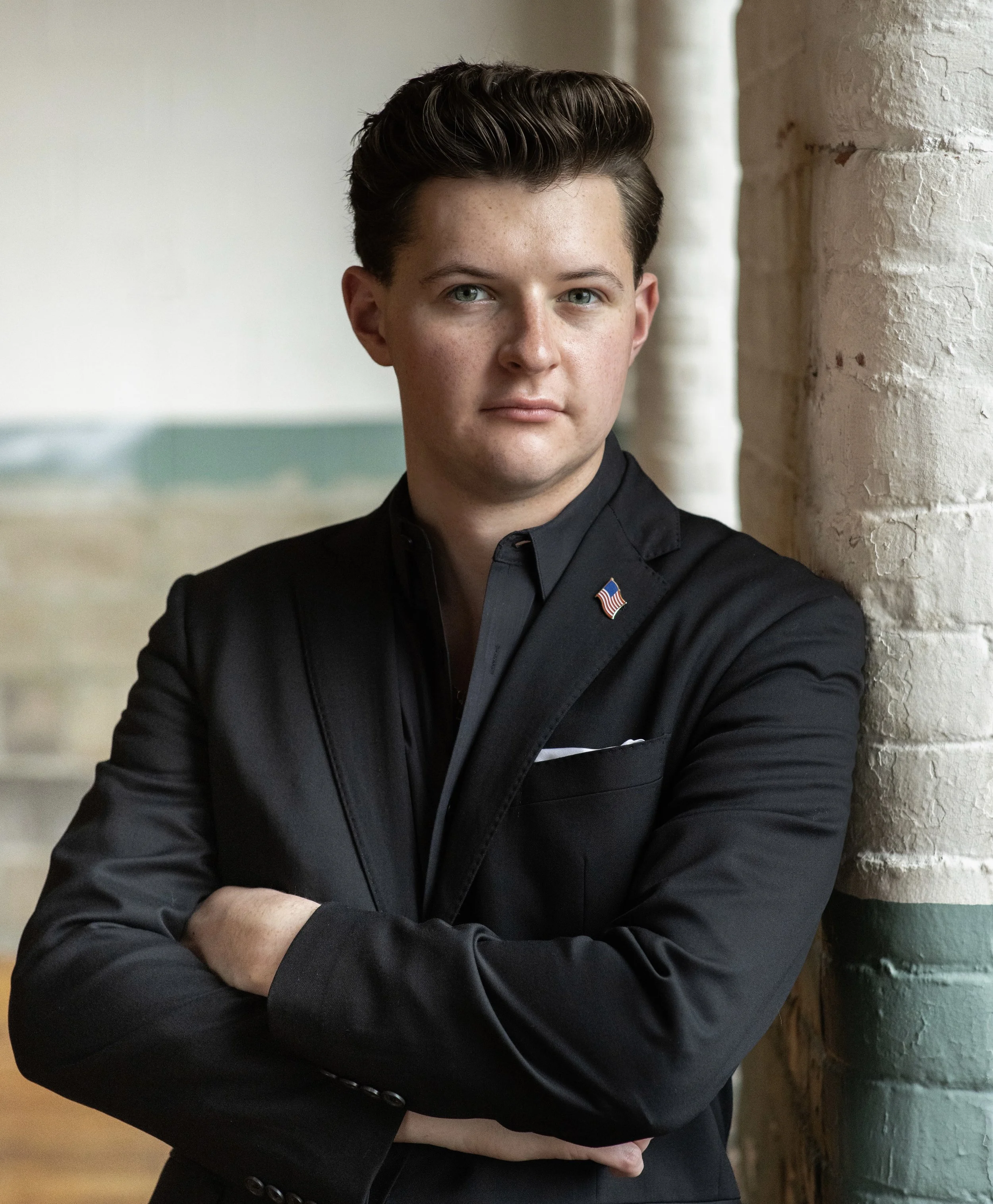 Portrait of a person in formal attire standing against a brick wall.