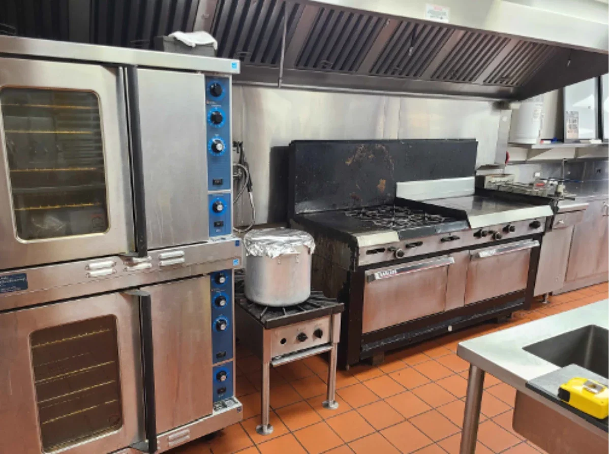 Commercial kitchen with oven, stove, and exhaust hood.