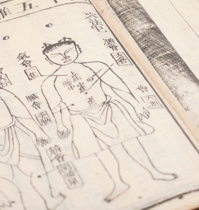 Close-up of an ancient Traditional Chinese Medicine (TCM) text featuring a hand-drawn anatomical diagram of a human figure, marked with acupuncture points and meridians, alongside Chinese characters on aged paper.