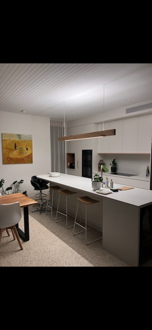 Modern kitchen interior with white cabinets, a long island with stools, pendant lighting, wall art, and plants.