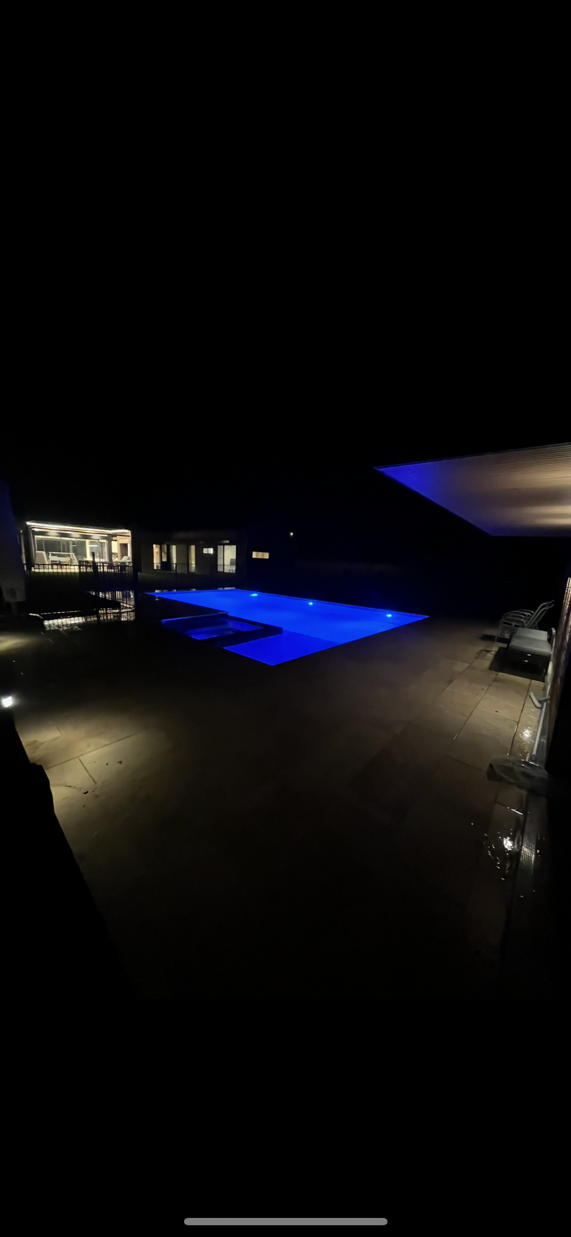 Illuminated pool at night with surrounding deck and seating area.