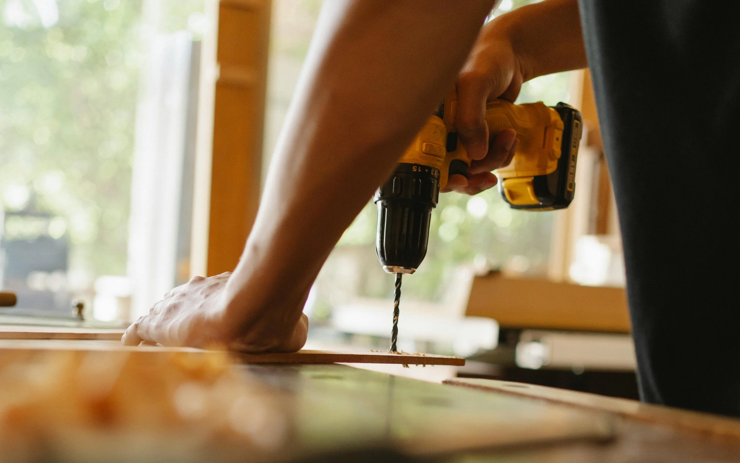 Person using a cordless drill on a piece of wood indoors.