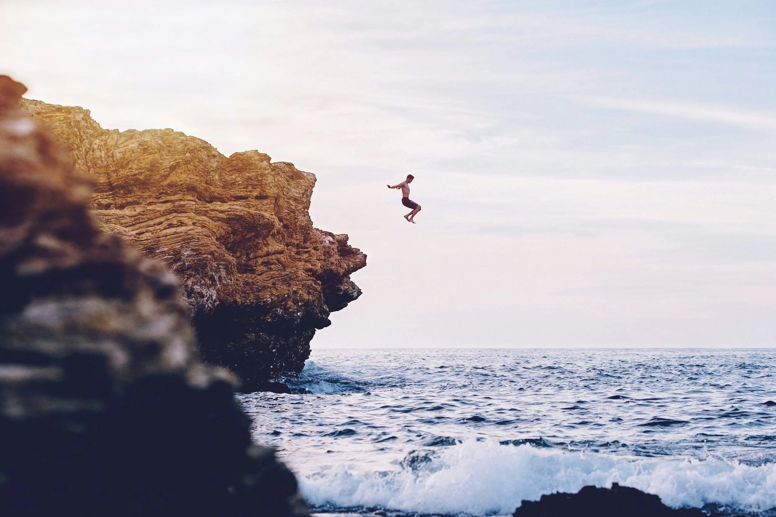 Man jumping off cliff into ocean