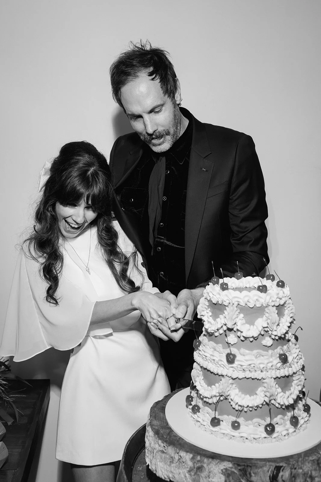 A man and woman cutting a wedding cake together, both smiling and excited, at a celebration event.