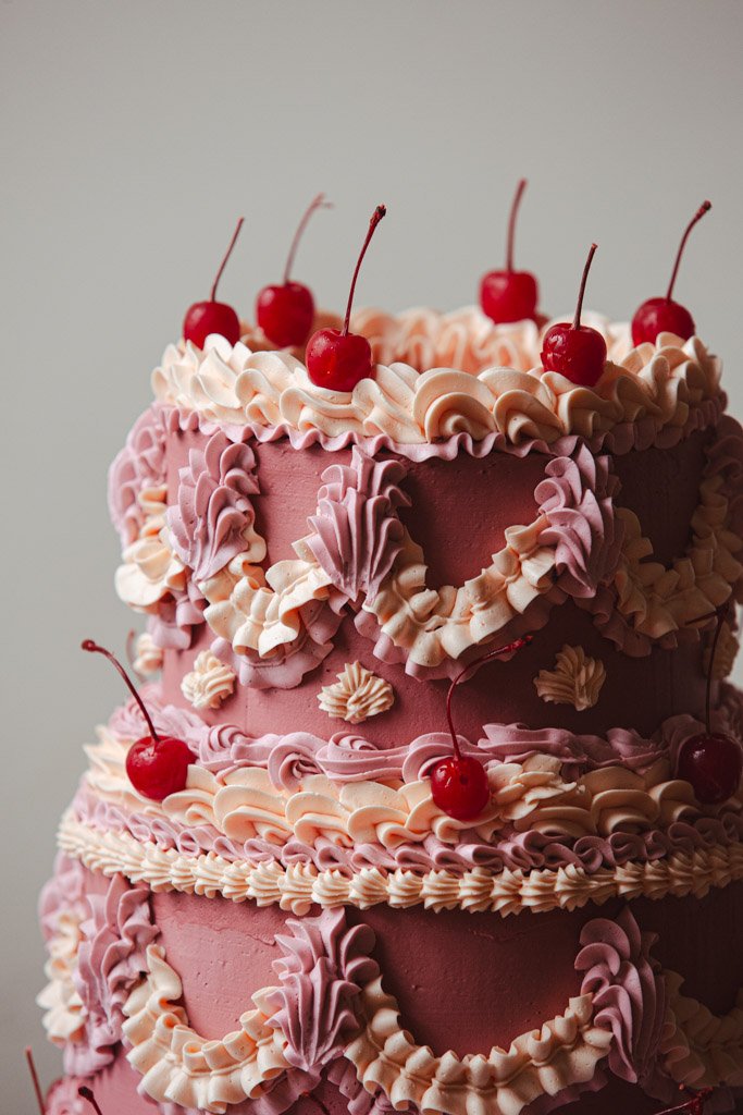 A pink frosted layered birthday cake decorated with whipped cream and fresh cherries.