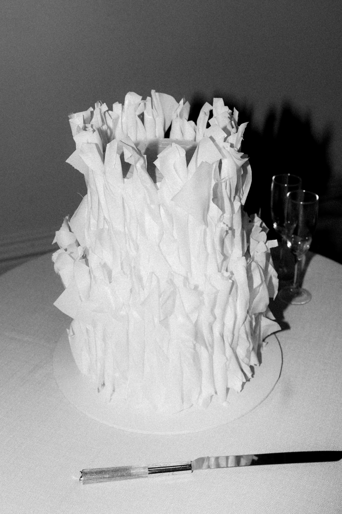 A decorative paper lantern with crumpled, textured paper around the exterior, sitting on a table. Two empty champagne glasses are placed beside it, and a sharp knife with a textured handle is in the foreground.