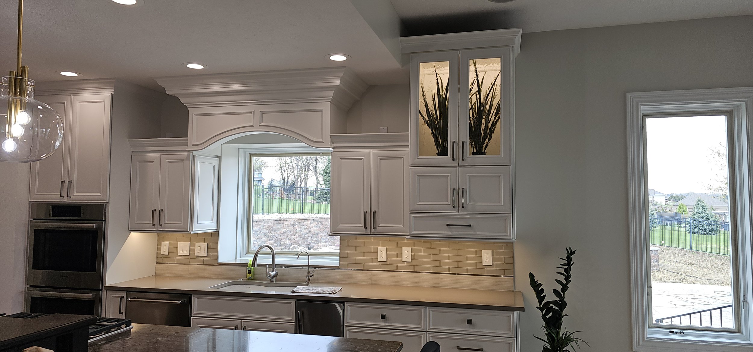 Modern kitchen with white cabinetry, stainless steel appliances, a window with a view of a yard, and a hanging light fixture. Under cabinet lights.